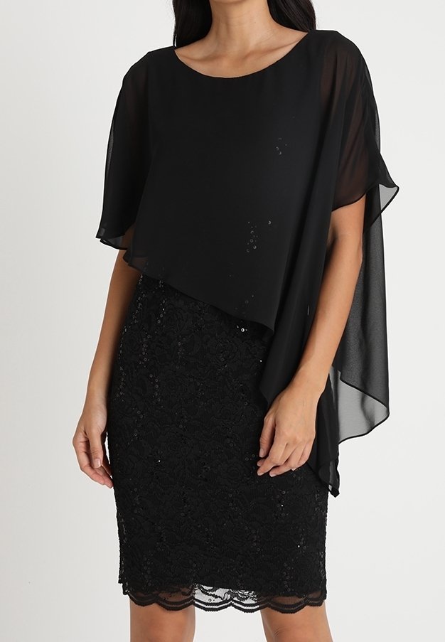 Femme portant une jupe en dentelle noire mi-genou avec un ourlet festonné et un haut noir ample, transparent, asymétrique avec des manches courtes.