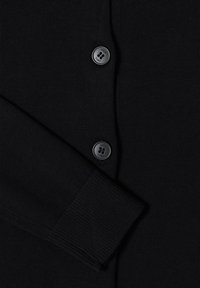 Manche de cardigan en maille noire reposant sur le devant boutonné avec deux boutons noirs à quatre trous visibles.