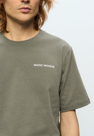 Olive rohe puuvillane T-särk, ümar kaelus, lühikesed varrukad ja rinnal valge "WOOD WOOD" logo. Sile tekstuur.