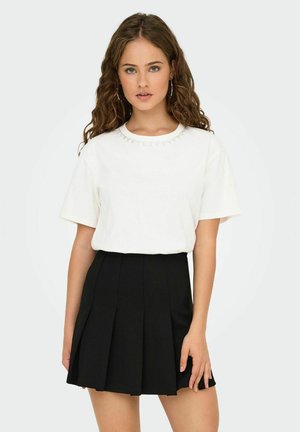 T-shirt blanc à manches courtes avec un col décoratif en perles, associé à une jupe plissée noire taille haute. Texture de tissu lisse.