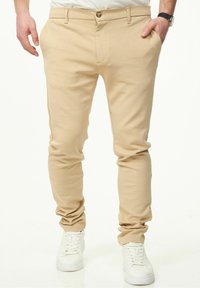 Beige Chinos im Slim-Fit, mit Knopfverschluss und Seitentaschen, kombiniert mit weißen Sneakers. Geschmeidige Stofftextur.