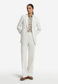 Vit texturerad kostym med en skräddarsydd kavaj och vida byxor, kombinerad med en ljusbrun randig blus och bruna sandaler.