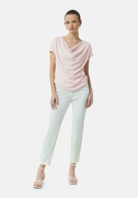 Helles rosa drapiertes Oberteil mit einem Cowlenkragen, kombiniert mit schlanken weißen Hosen und weißen, schnallen Sandalen. Glatte Textur, minimalistisches Design.