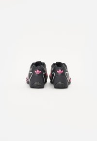 Svarte treningssko med rosa detaljer, teksturert overflate, glatt design og gummisåle. Har et signaturlogo på hælen.