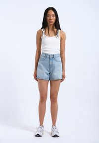 Shorts en denim bleu clair taille haute avec une coupe décontractée, cinq poches et un léger délavage, associés à un débardeur blanc ajusté et des baskets.