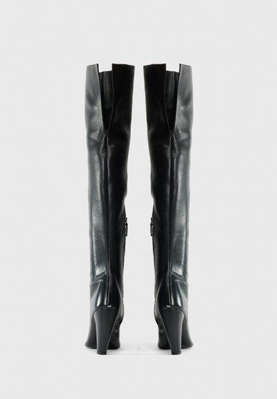 Knee-high black leather boots with a sleek design, pointed toe, and high heel. Features a cutout detail at the top and side zippers.