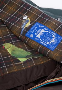 Πράσινο και καφέ καρό μπουφάν με μπλε ετικέτα, που διαθέτει απεικονίσεις ενός μπλε τσίχλου και ενός πράσινου παπαγάλου. Υφασμα με υφή και αντίθετες λεπτομέρειες.