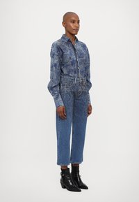 Blue patterned denim shirt with long sleeves, paired with light blue straight-cut jeans. Black ankle boots complete the outfit.