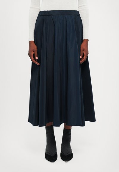 Gonna midi blu navy con pieghe, vita elasticizzata e texture liscia. Abbinata a calze grigie e scarpe nere a punta.