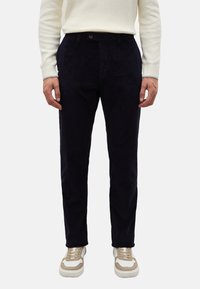 Marineblauwe corduroy broek met verticale geribbelde textuur, voorzien van een knoopsluiting en zijzakken, gecombineerd met beige sneakers.