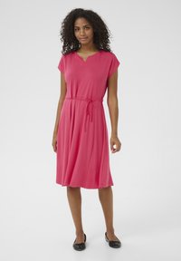 Robe rose en tissu doux, avec un décolleté en V, des manches courtes et une taille à cordon pour un ajustement réglable. La jupe évasée tombe sous le genou.