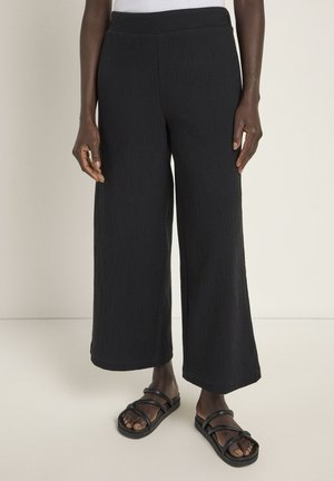 Black wide-leg pants made from textured fabric with a ribbed design. Features an elastic waistband. Paired with black strappy sandals.