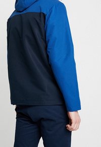 Blue and black hooded jacket, featuring a contrasting upper panel, smooth texture, and elastic cuffs. Simple design, functional style.