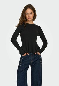 Pull-over noir à manches longues avec une coupe décontractée et une texture côtelée. Associé à un jean en denim taille haute avec des détails lacés sur les côtés.