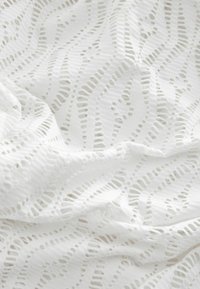Tissu en dentelle blanche présentant un motif en vagues avec des découpes. La texture est aérienne, lisse et délicate, idéale pour des vêtements ou un usage décoratif.