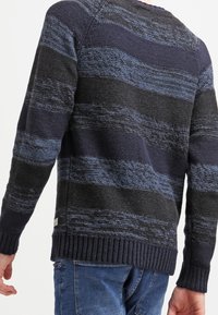 Sweter dzianinowy z poziomymi paskami w ciemnym granacie i niebieskim kolorze, teksturowana tkanina, ściągacz na dole oraz małe haftowane logo z boku.