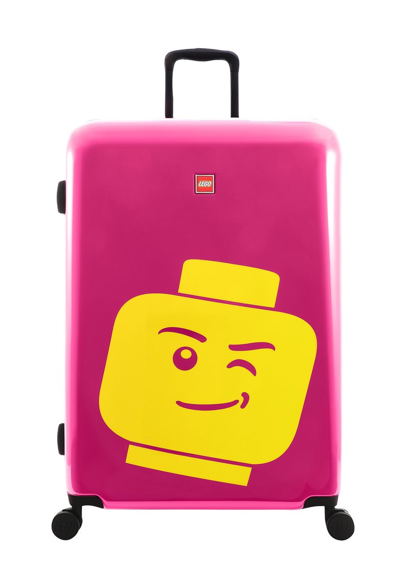 Hard-shell suitcase in bright pink with a large yellow LEGO figure face design. Features a black retractable handle and wheels.