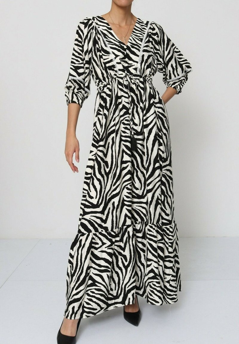 Robe maxi en imprimé zèbre noir et blanc. Présente un design croisé, des manches bouffantes, une ceinture à nouer et un ourlet à volants en couches.