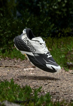 Schwarz-weißer Sportschuh mit strukturierter Oberseite, dicker Sohle und sichtbar angebrachtem Logo. Zeigt ein leichtes Design, ideal zum Laufen.