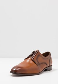 Brown leather dress shoe with polished finish, lace-up design, round toe, and stitched accents on the sides. Low stacked heel.