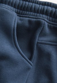 Tumesinised dressipüksid, mis on valmistatud pehmest ja tekstuurse kangaga, varustatud elastse vöökohaga ja küljetaskuga. Näha on tugevdusõmblusi.