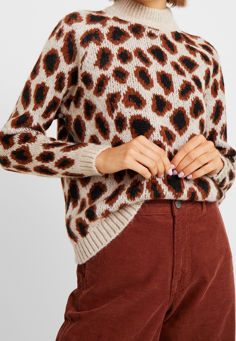 Strickpullover mit beigem Grundton und rostfarbenen sowie schwarzen Leopardenflecken, gerippter Hals- und Saumabschluss, kombiniert mit rostfarbener Cordhose.