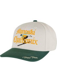 Căciulă bej cu brâu verde. Prezintă un text brodat "Monoski Chamonix" și un grafic cu un schior. Cusături de accent în galben și albastru.