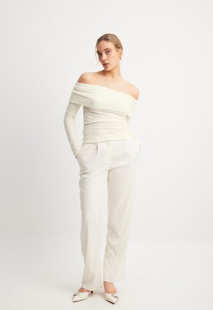 Off-shoulder, gestructureerde ivoorkleurige top met lange mouwen, gecombineerd met losse, crèmekleurige hoge taillebroeken en scherpe witte schoenen.