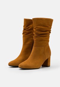 Bottes chelsea en suède beige avec un design flou, bout pointu et un talon carré, dotées d'une fermeture éclair sur le côté et d'une texture lisse.