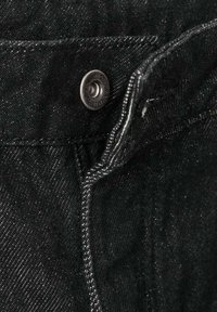 Tela de mezclilla negra con un botón de metal y costuras blancas contrastantes. La vista en primer plano resalta la textura y los detalles de las costuras.