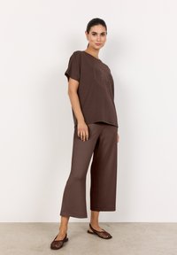 Braunes Set bestehend aus einem lässigen Kurzarmoberteil mit einem kreisförmigen Grafikmuster und weit geschnittenen Hosen. Strukturierter, leichter Stoff.