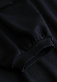 Gros plan sur une manche en tissu noir avec un poignet élastique froncé et des coutures visibles.