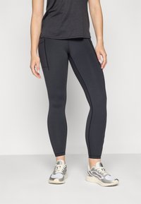 Leggings negre, ajustate, cu o textură netedă, cusături planificate și buzunare laterale. Asortate cu adidași gri și albi.