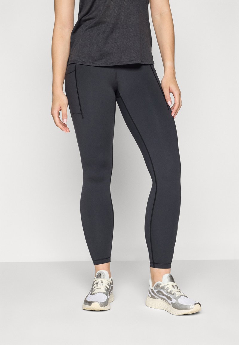 Leggings negre, ajustate, cu o textură netedă, cusături planificate și buzunare laterale. Asortate cu adidași gri și albi.