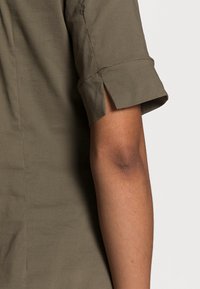 Korte mouwen overhemd in olijfgroen stof met een relaxte pasvorm. Opvallende kenmerken zijn de opgerolde manchetten en een zachte, gladde textuur.