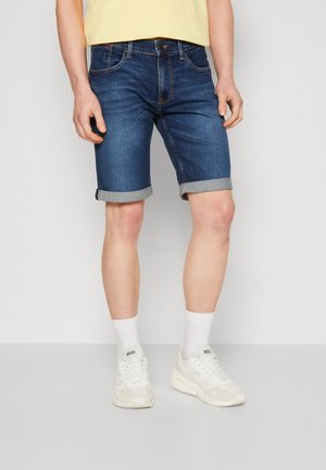 Shorts di denim blu scuro con un classico design a cinque tasche, orli risvoltati e una texture liscia, abbinati a scarpe da ginnastica bianche e calzini.