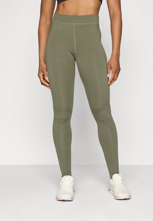 Hoch-taillierte, dehnbare Leggings in Olivgrün, mit einer glatten Textur und flachen Nähten, kombiniert mit leichten Sportschuhen.