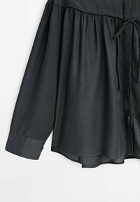 Zwarte, lichte blouse met een losse pasvorm, voorzien van een geraffineerde taille en lange mouwen, knoopsluiting aan de voorkant en een stoffen strikaccent.