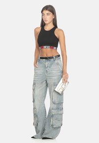 Top corto nero con logo "DIESEL" rosso, abbinato a jeans cargo larghi blu chiaro con molte tasche e una pochette argentata.