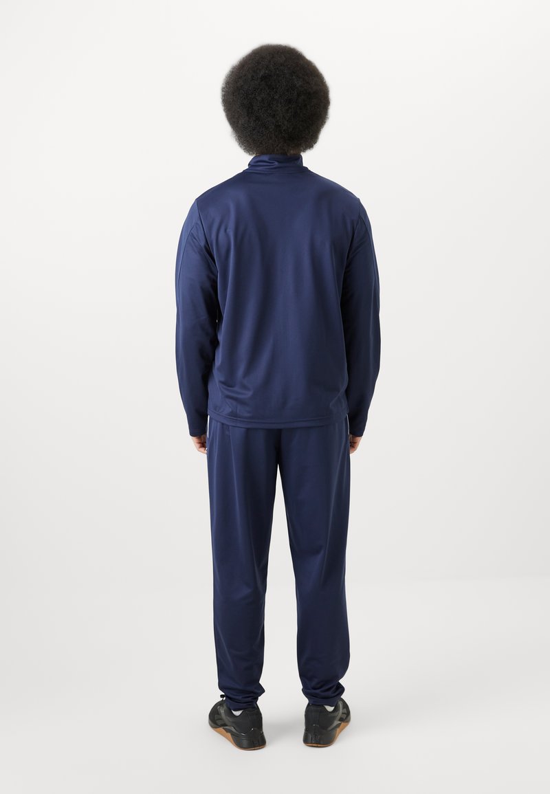 Chándal deportivo en azul marino hecho de una tela suave, con cuello alto, mangas largas y pantalones a juego, combinado con zapatillas negras.