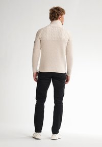 Maglione a cable-knit crema con colletto alto e texture a coste, abbinato a pantaloni neri e scarpe bianche. Vista da dietro.