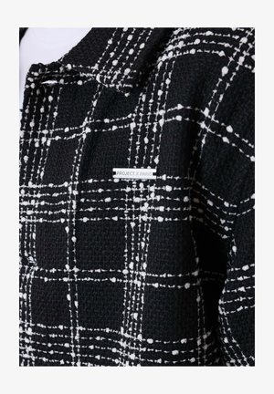 Black textured jacket with white checkered pattern and a small metal label reading "PROJECT X PARIS" on the chest area.