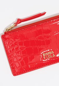 Cartera de charol roja con textura de cocodrilo, cremallera dorada y logo grabado. Cuenta con un asa de muñeca y detalle de costura.