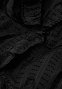 Zwarte stoffen top met textuurpatronen, geschulpte halslijn en decoratieve accenten. Materiaal lijkt zacht met een gelaagde constructie.