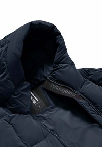 Marineblauwe pufferjack met een hoge kraag, gestructureerde stof, branding op de rits en een gevoerde binnenkant voor warmte.