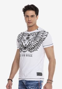 Weißes T-Shirt mit einem großen schwarzen Löwenmotiv und Flügeln, rundem Ausschnitt, kurzen Ärmeln und einem schwarzen Etikett am Saum.