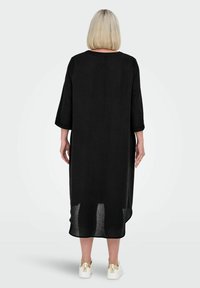 Vestito nero al ginocchio con maniche a tre quarti, scollatura rotonda e orlo trasparente. Indossato con sneakers bianche con dettagli dorati.