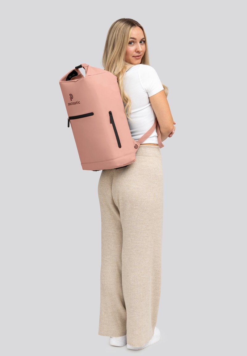 Mochila impermeable rosa con cremalleras negras y una correa ajustable, que presenta una parte superior redonda y un logo minimalista en la parte frontal.