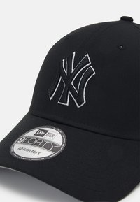 Schwarze Baseballmütze aus Stoff mit einem gestickten weißen New York Yankees Logo auf der Vorderseite und einem runden Markenaufkleber auf dem Schirm.