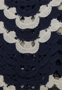 Tessuto all'uncinetto caratterizzato da motivi a scaglie alternati in blu navy e crema, con una finitura texture e un design a traforo.